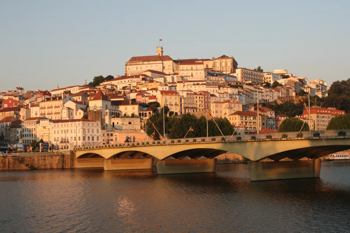 Coimbra's old town rising in warm evening light above the arches of a bridge over the Mondego River